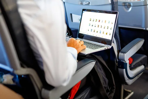 Неузнаваемый молодой бизнесмен с ноутбуком, сидящим в самолёте — стоковое фото