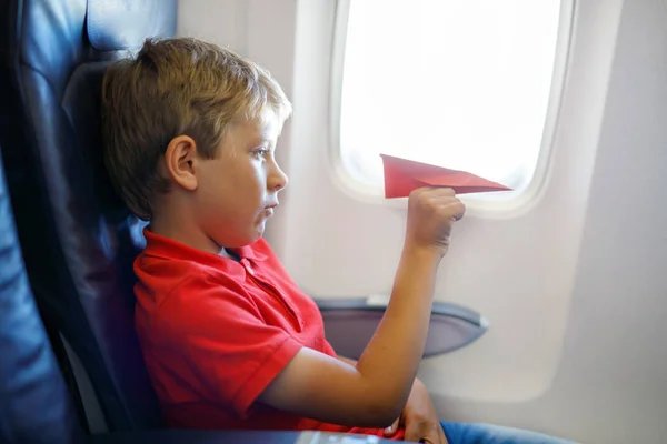Маленький мальчик играет с красной бумагой самолет во время полета на самолете — стоковое фото