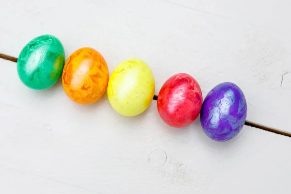 Paaseieren op houten achtergrond. Kleurrijke eieren in verschillende kleuren - rood, geel, oranje, paars en groen. — Stockfoto