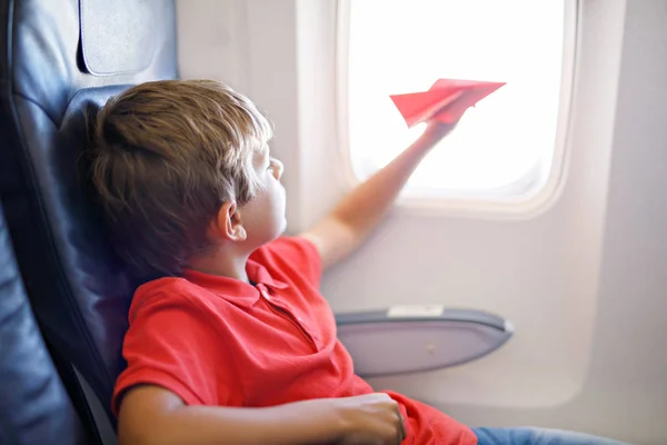 Niño jugando con avión de papel rojo durante el vuelo en avión — Foto de Stock