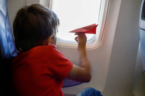 Niño jugando con avión de papel rojo durante el vuelo en avión — Foto de Stock