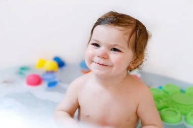 Küvette köpüklü banyo yapan sevimli, sevimli bir kız. Bebek banyo lastiğiyle oynuyor..