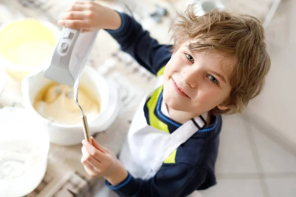 Beautiful funny blond little kid boy baking chocolate cake and tasting dough in domestic kitchen — Stock Photo, Image