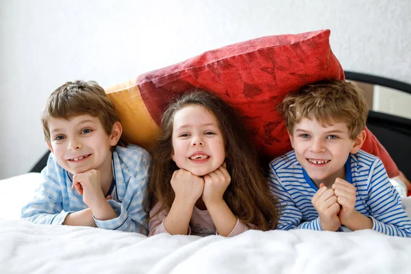 Τρία χαρούμενα παιδιά με πιτζάμες γιορτάζουν το πυτζάμα πάρτι. Νηπιαγωγεία και σχολεία αγόρια και κορίτσια διασκεδάζουν μαζί — Φωτογραφία Αρχείου