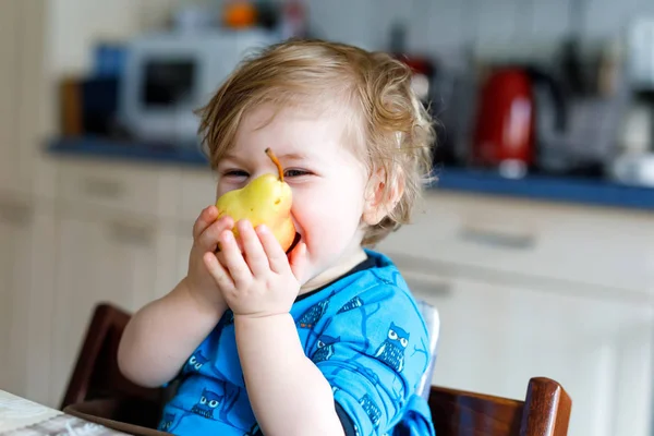 Χαριτωμένο κοριτσάκι που τρώει φρέσκο αχλάδι. Πεινασμένο χαρούμενο μικρό παιδί ενός έτους που κρατάει φρούτα. — Φωτογραφία Αρχείου