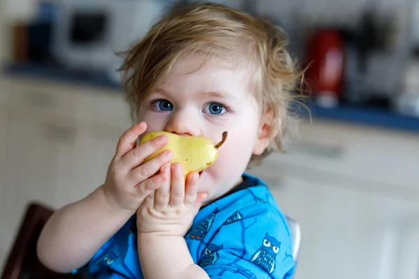 Linda adorable niña comiendo pera fresca. Bebé feliz hambriento de un año sosteniendo fruta. — Foto de Stock