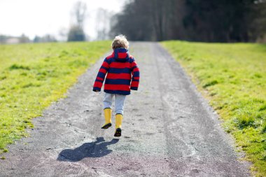 Küçük sarı yağmur botları ve sıcak güneşli yolda Doğa bahar günü yürüyüş çocuk çocuk.