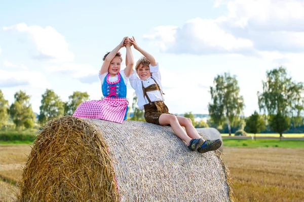 Two kids, boy and girl in traditional Bavarian costumes in wheat field with hay bales — Stock Photo, Image