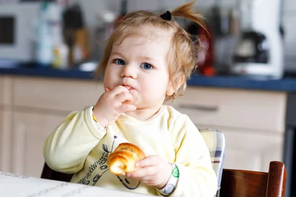 Boldog kislány, aki friss croissant-t eszik reggelire vagy ebédre. Egészséges táplálkozás gyermekek számára — Stock Fotó