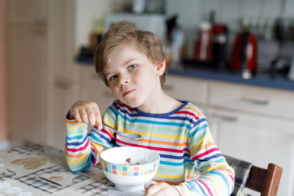 Glad liten blond kid pojke äter spannmål för frukost eller lunch. Hälsosam kost för barn. — Stockfoto