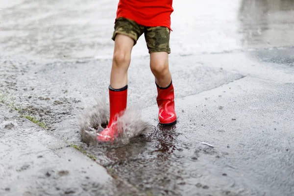 Bir su birikintisi içine atlamak Kızıl yağmur giyen çocuk botları. — Stok fotoğraf