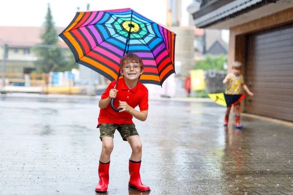 Jongen jongen dragen rode regen laarzen en wandelen met paraplu — Stockfoto