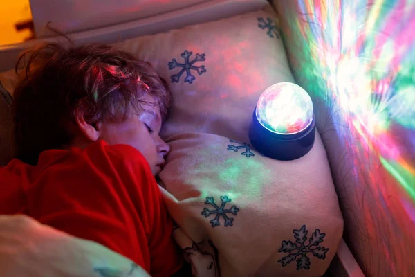Little preschool kid boy sleeping in bed with colorful lamp.