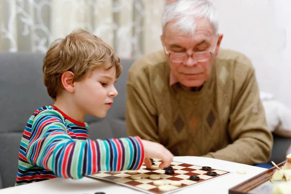 Beetje kid jongen en senior grootvader samenspelen checkers spel — Stockfoto