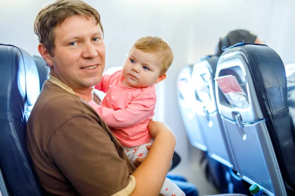 Молодой уставший отец и его плачущая маленькая дочь во время полета на самолете собирается в отпуск — стоковое фото