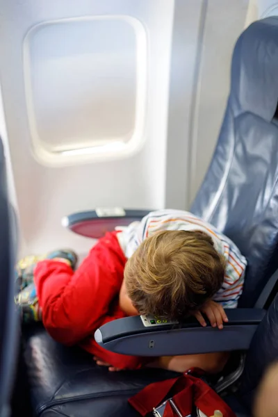 Kleiner Junge schläft während des langen Fluges im Flugzeug. Kind sitzt im Flugzeug am Fenster — Stockfoto