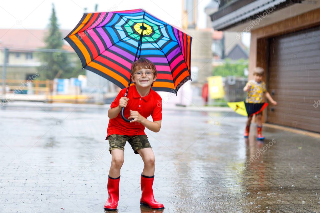 Kid boy wearing red rain boots and walking with umbrella