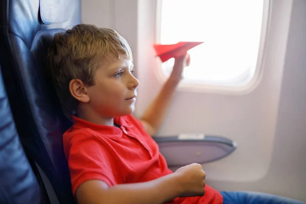 Niño jugando con avión de papel rojo durante el vuelo en avión — Foto de Stock