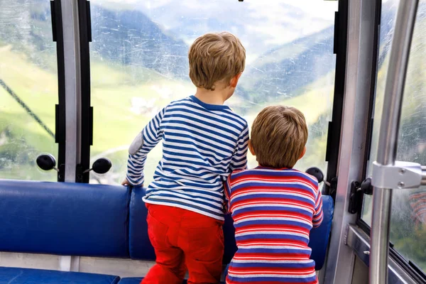 Two little boys sitting inside of cabin of cable car and looking on mountains landscape. — Stock Photo, Image