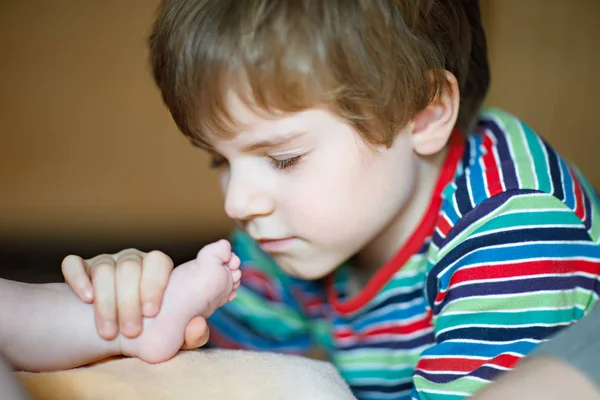 Little kid boy kissing and playing with foot of newborn baby. — Stock Photo, Image