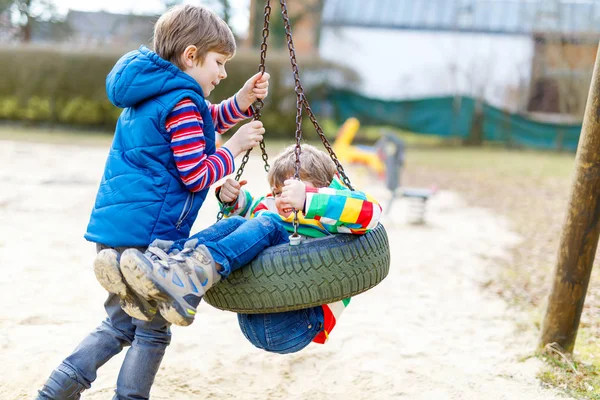 Dos niños pequeños que se divierten con el oscilación de la cadena en el patio al aire libre — Foto de Stock