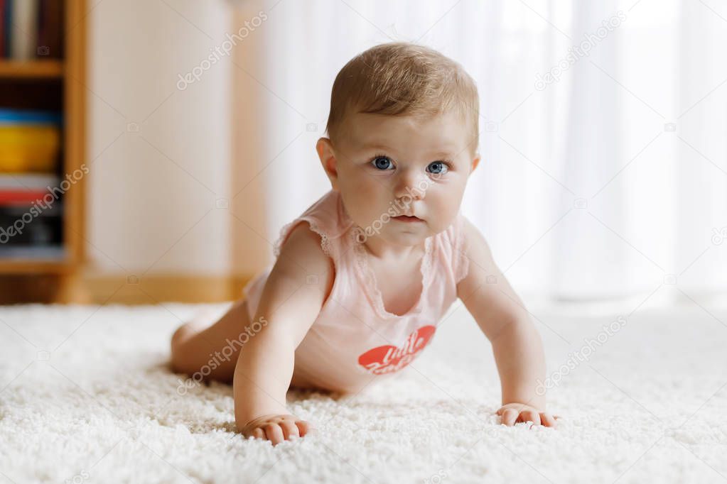 Little funny baby girl lifting body and learning to crawl.