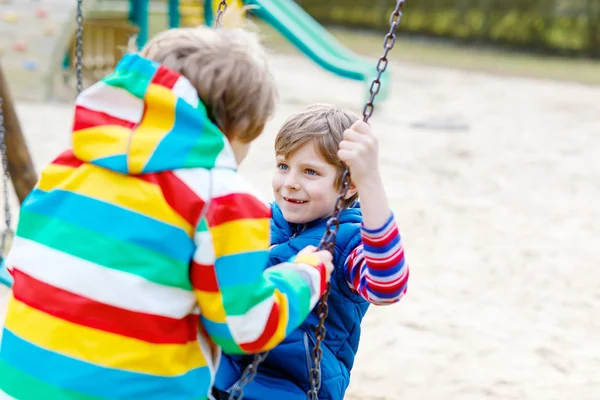 Two little kid boys having fun with chain swing on outdoor playground — Stock Photo, Image