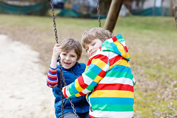 Two little kid boys having fun with chain swing on outdoor playground — Stock Photo, Image