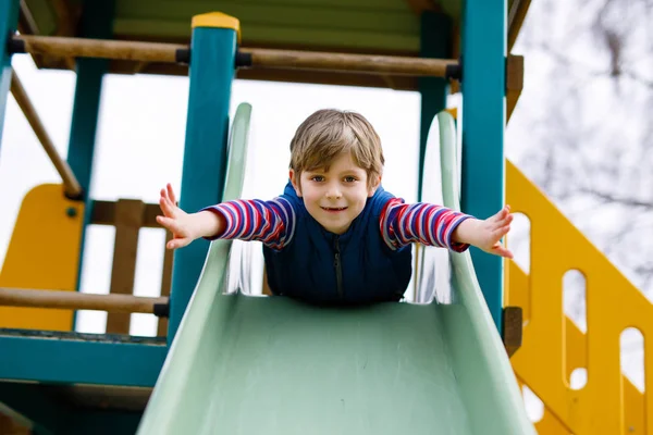 Happy blond kid boy having fun and sliding on outdoor playground — Stock Photo, Image