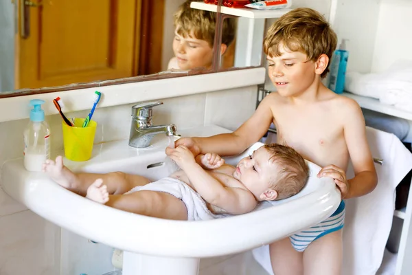 Cute adorable baby taking bath in washing sink and grab water tap. — Stock Photo, Image