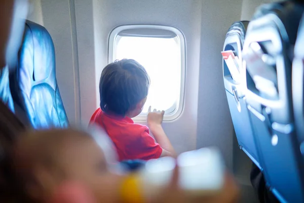 Mały chłopiec dziecko szuka poza okna samolotu podczas lotu na samolocie. — Zdjęcie stockowe