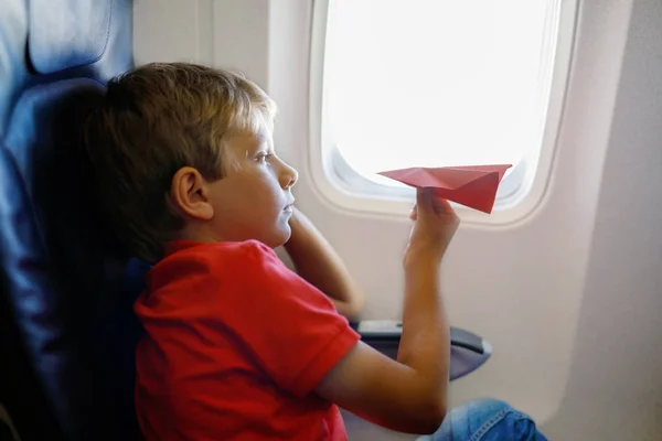 Niño jugando con avión de papel rojo durante el vuelo en avión — Foto de Stock