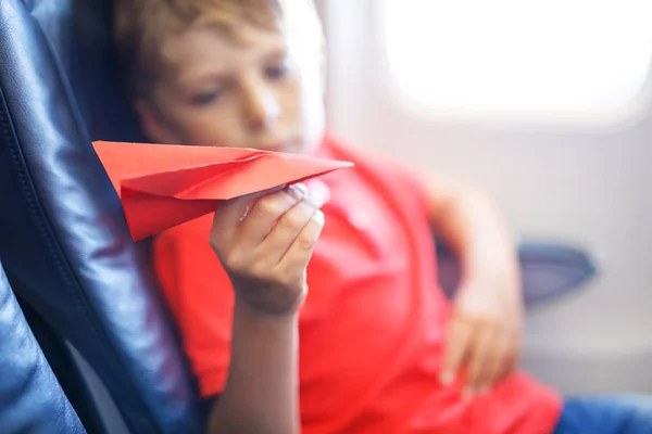 Kleine jongen jongen spelen met rood papier vliegtuig tijdens de vlucht op vliegtuig — Stockfoto