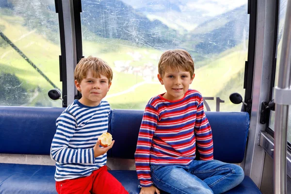 Dois garotinhos sentados dentro da cabine do teleférico e olhando para a paisagem das montanhas . — Fotografia de Stock