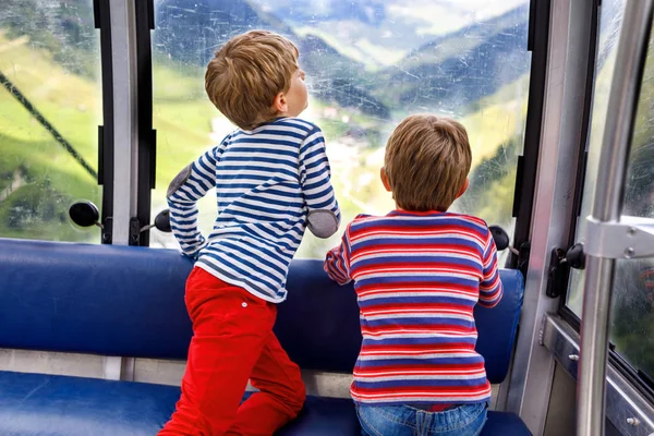 Dois garotinhos sentados dentro da cabine do teleférico e olhando para a paisagem das montanhas . — Fotografia de Stock