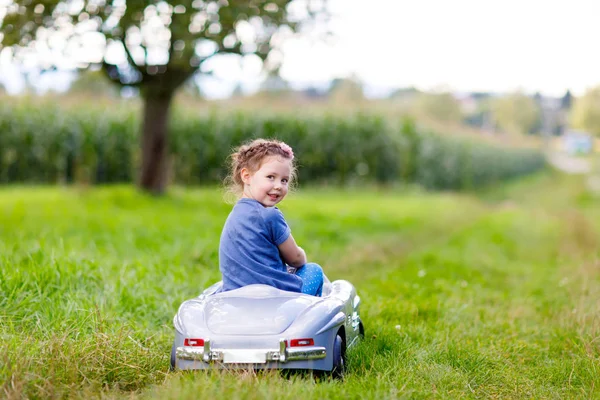 Κοριτσάκι προσχολικής ηλικίας το παιδί κάθεται στο παλιό αυτοκίνητο μεγάλο παιχνίδι και τη διασκέδαση στην ηλιόλουστη καλοκαιρινή μέρα — Φωτογραφία Αρχείου