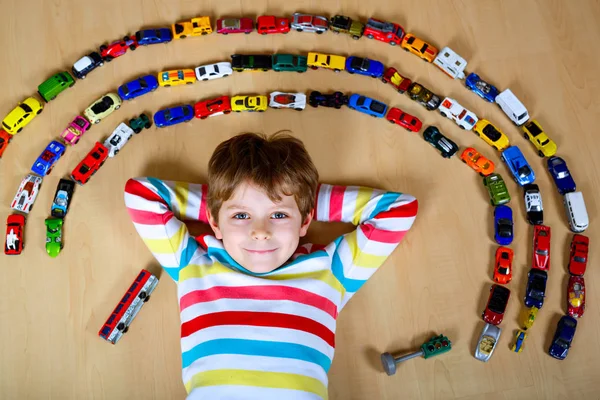 Bonito menino loiro brincando com lotes de carros de brinquedo interior . — Fotografia de Stock