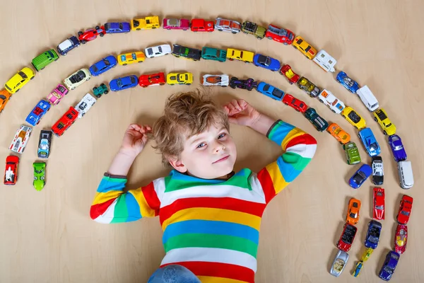 Lindo niño rubio pequeño jugando con un montón de coches de juguete interior . — Foto de Stock