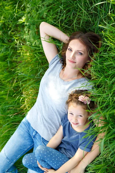 Красивая молодая мать и маленькая дочь лежат на зеленой траве и отдыхают — стоковое фото