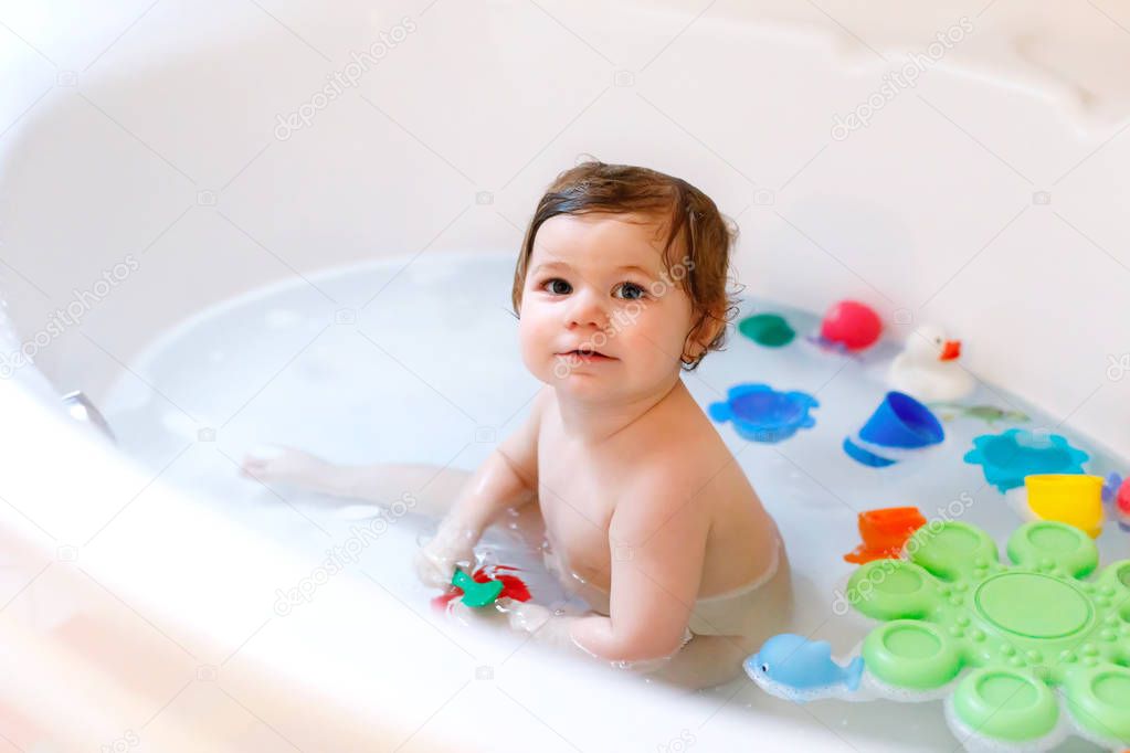 Cute adorable baby girl taking foamy bath in bathtub. Toddler playing with bath rubber toys.