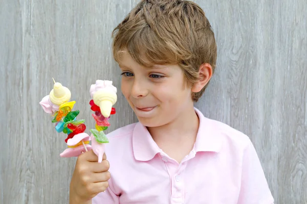 Happy little kid boy holding marshmallow skewer in hand. Child with different unhelthy colorful sweets — Stock Photo, Image