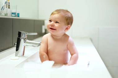 Lavaboda yıkanan, su ve köpükle oynayan sevimli bir bebek.