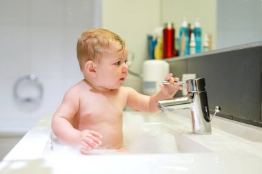 Lavaboda yıkanan, su ve köpükle oynayan sevimli bir bebek.