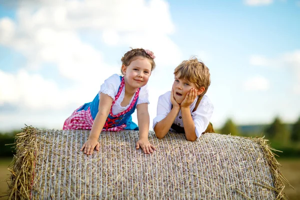 Two kids, boy and girl in traditional Bavarian costumes in wheat field with hay bales — Stock Photo, Image