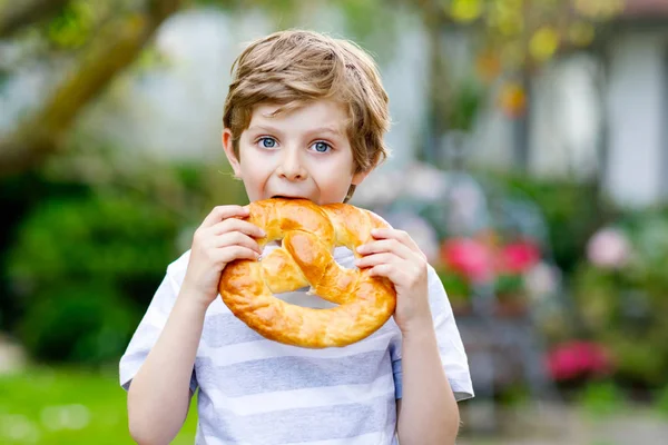 Uroczy mały chłopiec jedzący wielkiego bawarskiego niemieckiego precla. — Zdjęcie stockowe