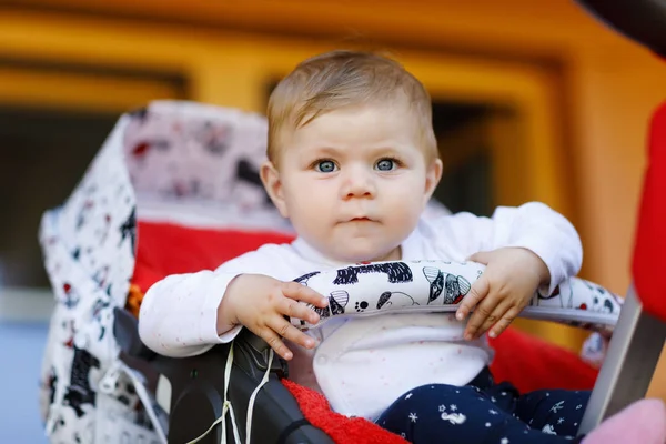 Bonito menina bonita sentada no carrinho de bebê ou carrinho e esperando a mãe. Criança sorridente feliz com olhos azuis . — Fotografia de Stock