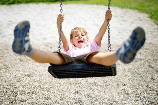 Αστείο παιδί αγόρι έχοντας διασκέδαση με αλυσίδα swing στην υπαίθρια παιδική χαρά ενώ είναι υγρό πιτσιλιστεί με νερό — Φωτογραφία Αρχείου