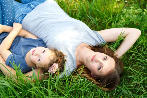 Красивая молодая мать и маленькая дочь сидят на зеленой траве и отдыхают — стоковое фото