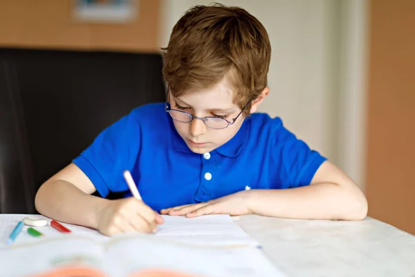 Anak kecil yang lucu berkacamata di rumah membuat PR, menulis surat dengan pena berwarna-warni . — Stok Foto