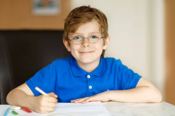 Schattige kleine jongen jongen met bril thuis maken van huiswerk, het schrijven van brieven met kleurrijke pennen. — Stockfoto